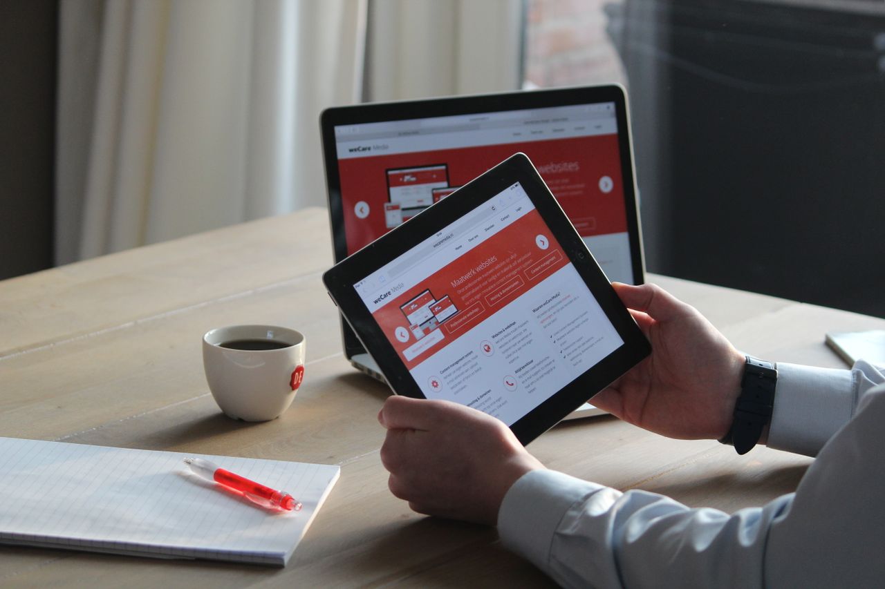 Business professional using a tablet and laptop with a hot drink, focusing on digital content review.